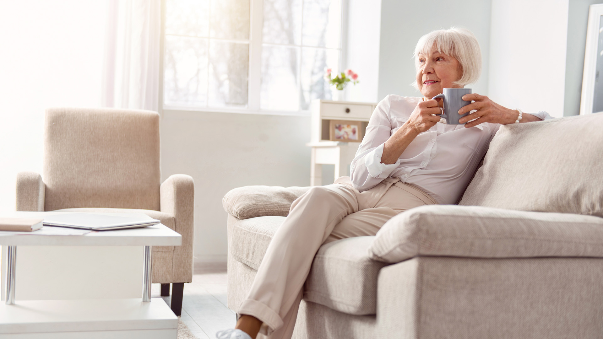 Petite elderly woman drinking coffee in her living room
