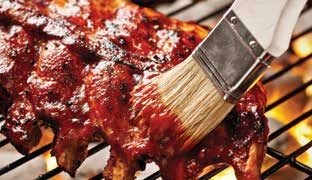 a marinating brush rubbing bbq sauce onto a rack of ribs sitting atop a charcoal grill